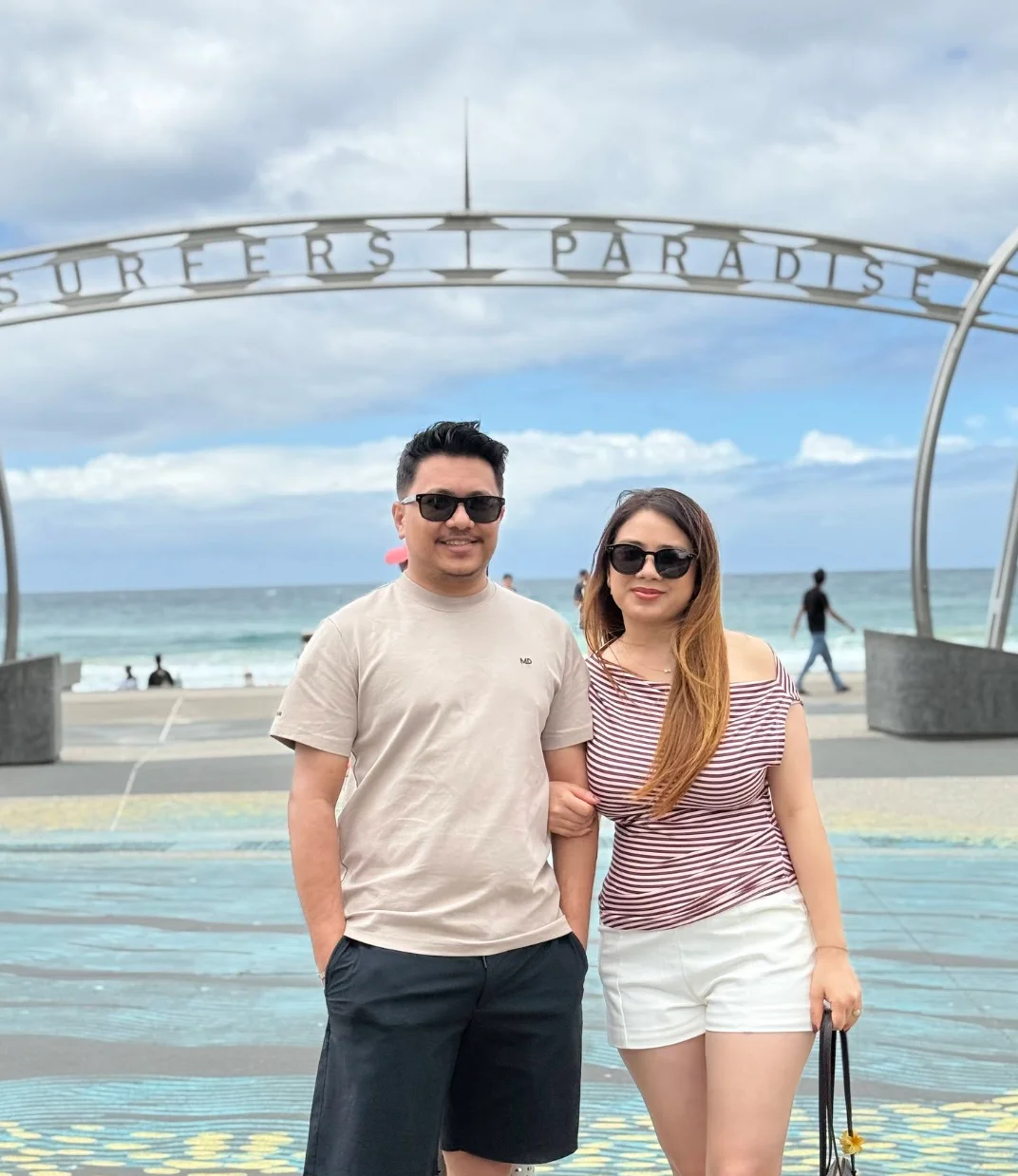 Suyog and Susmita beneath the Surfers Paradise sign with the beach behind them