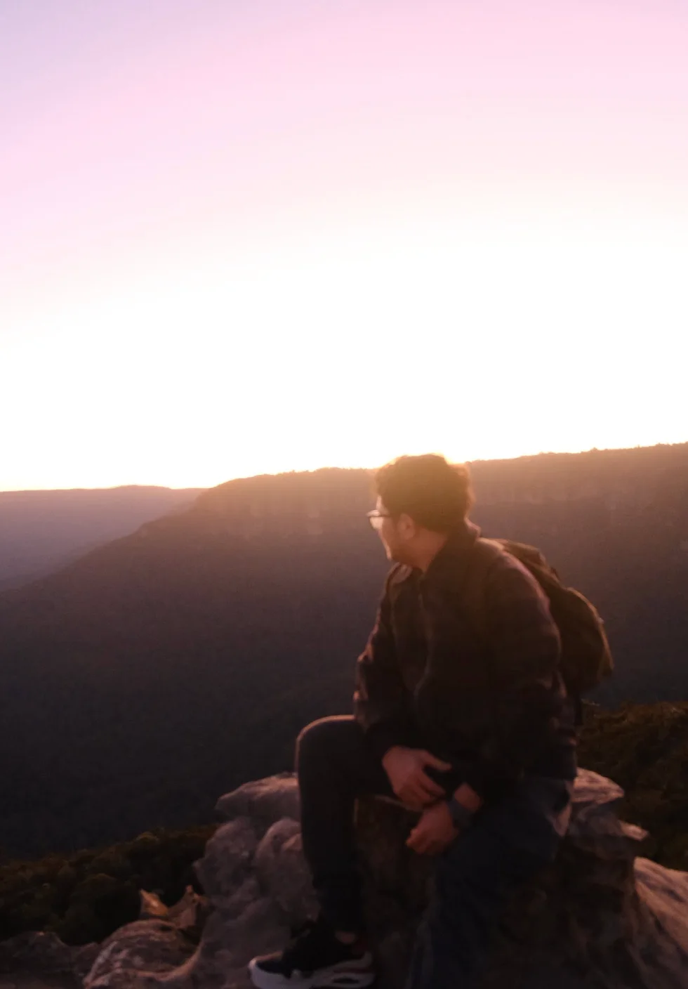 Suyog sitting on rocks overlooking mountains beneath a pink sky